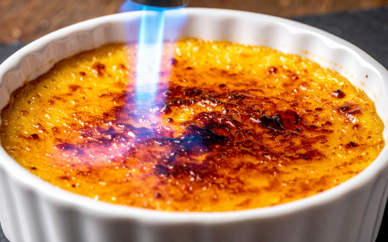 4 Close-up of torch flame caramelizing sugar on crème brûlée, highlighting the beloved burnt top of this classic French dessert.